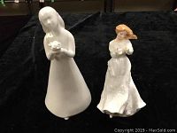 White and colored Royal Doulton figurines photographed from front on a black background