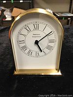 Front view of gold-tone quartz clock with Roman numeral dial and Tiffany & Co Portfolio branding.