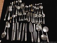Full view of 42-piece vintage silver-plated cutlery set including knives, serving utensils, and souvenir spoons arranged on a black surface.