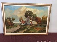 Framed oil painting showing rural landscape with white houses and trees.