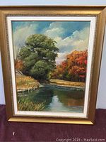 Framed oil on canvas landscape painting showing detailed river scene and trees in autumn colors.