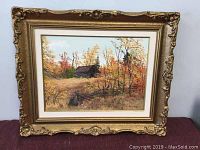 Full view of framed oil painting depicting an autumn landscape with a cabin surrounded by colorful trees in fall foliage.