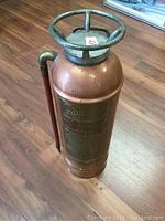 Full view of the copper fire extinguisher showing cylindrical shape, top handle, and discharge tube.