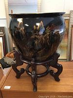 Front view of the black ceramic jardiniere with hand-painted Asian motifs on wooden stand