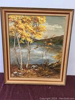Full view of framed oil painting depicting autumn landscape with birch trees and lake.