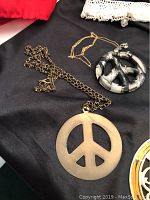 Photo of two large peace sign pendant necklaces and a gold-tone abstract circular pendant necklace.