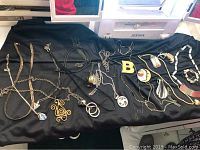 Overhead view of assortment of costume necklaces and pendants on black fabric laid over a white surface under daylight