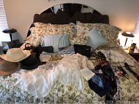 Wide view of all scarves, hats, purses, and accessories displayed on floral patterned bedspread with pillows in background.