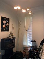 Tall brass floor lamp with five adjustable dome-shaped light fixtures illuminating a corner near window and furniture.