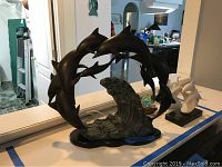 Front view of hollow metal dolphin and wave sculpture on oval base, showing multiple dolphins