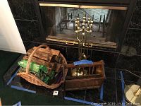 Wide view of fireplace area showing basket with firewood, starter logs, lighters, wood magazine rack, and brass fireplace tool set including shovel, poker, tongs, and broom.