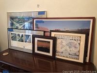Five framed pictures on a table including Madison Wisconsin Badgers football field aerial photo, four smaller Badgers field images, a bridge photo at sunset, and a vintage world map.