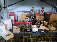 Shelf with various Christmas decoration items including boxed ornaments, nutcrackers, mugs, water globe, and small tree