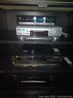 Photo showing multiple electronic components on shelves, including Sony tape player and Cisco receiver with digital clock display.