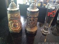 Photo showing two detailed German beer steins with pewter lids and one tall Michael Jordan Chicago Bulls stitched glass stein