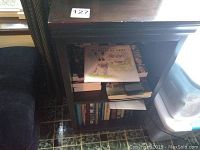 Front and side view of dark brown two-shelf wooden bookcase showing shelves with books and other items.