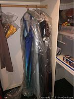 Photo of multiple dresses hanging in a closet on a rod with some in protective plastic garment bags.