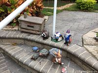 Wide shot of cedar bird box and seven assorted plastic composite garden figurines arranged on outdoor stone steps