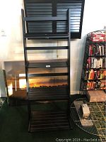Collapsible ladder style black wooden shelf shown upright with two stretched canvas prints leaning behind it on the floor.