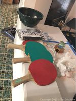 Ping pong paddles, black bowl with balls, boxed net, paddle cover, and small accessories on table