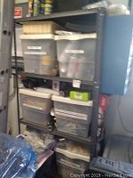 Metal shelving unit with multiple plastic tubs labeled 'Spray Paints' and 'Stain/Small Paint Cans/Tubes' containing spray paint and paint cans.