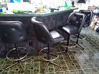 Four black leather-look kitchen bar stools with button tufting and metal bases with circular footrests at a counter.