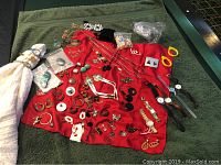 Full lot view showing variety of costume jewelry including earrings, rings, necklaces, and watches laid out on a red cloth.