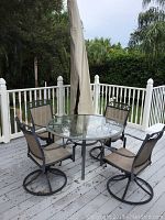 Three-quarter view of round table with glass insert, four chairs, and closed umbrella on deck