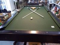 Full view of pool table with green felt, pool balls arranged in triangle, and two pool cues crossed on table