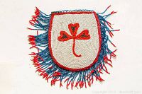 Front of the beaded Indigenous belt bag showing white bead background with red and black leaf pattern and blue and red beaded fringe.