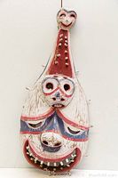 Full frontal view of the old indigenous wooden dance mask showing two vertically stacked faces with red, white, and blue paint, minor chips and wear.