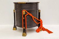 Front view of round black ribbed lacquered box on three legs with orange cord