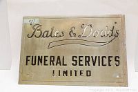 Full view of the rectangular metal sign showing 'Bates & Dodds Funeral Services Limited', lightly faded and scratched with mounting holes