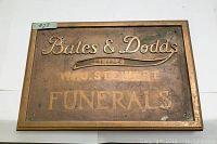 Rectangular bronze plaque with embossed lettering and patina, showing the full text 'Bates & Dodds', 'W.H.O. Stewart', and 'FUNERALS'.