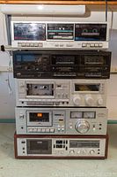 Full stack view of five vintage stereo cassette decks, showing front panels, buttons, cassette slots, display windows, tuning dials, and meters.