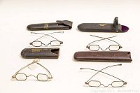 Four pairs of vintage eyeglasses arranged with their cases on display, showing frames and cases together.