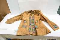 Full front view of tan moose hide coat laid flat showing floral bead panels, patch pockets and lower hem fringe
