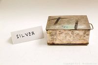 Three-quarter view of box showing overall shape, hinged lid, side handle and floral engraving