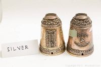Pair of conical sterling silver tzedakah boxes side by side showing different raised-relief motifs