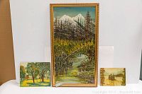 Group shot of all four signed paintings, largest framed mountain scene in center with three smaller paintings around it.