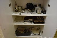 Overview of shelf containing meat grinder, baking pans, muffin tins, and box of cookie cutters in bottom shelf
