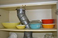 Vintage Pyrex mixing and casserole bowls on shelf, various colors, some with lids.