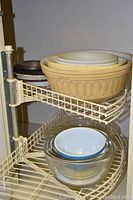 Various mixing bowls and pans stacked on a metal shelf rack, showing size variety and material mix including plastic, glass, and metal.