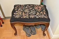 Top and side view of footstool showing needlepoint floral pattern on black fabric and carved wooden legs.