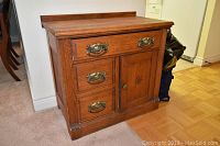 Front view of wooden washstand showing three drawers and one door with brass handles and knob