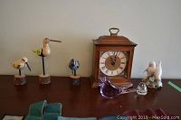 Wooden mantel clock with bird figurines including three wooden birds on log bases, two clear glass birds, and two white Royal Copenhagen dove figurines on a ceramic base.