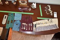Photo showing multiple silverplate souvenir spoons spread on table alongside small fork, knife, and cloth storage sleeves in different colors.