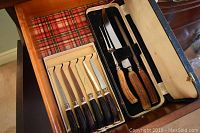 Set of steak knives and carving set displayed inside open drawers showing the knives' blades and handles distinctly.