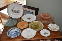 Collection of decorative plates of various sizes and materials placed on wooden surface.
