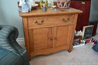 Full front view of the light wood washstand showing one top drawer with brass handles and two cabinet doors below with wooden knobs.